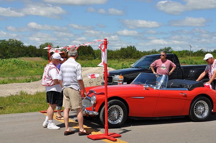 Red Austin Healey moves up to starting pole as workers look on.